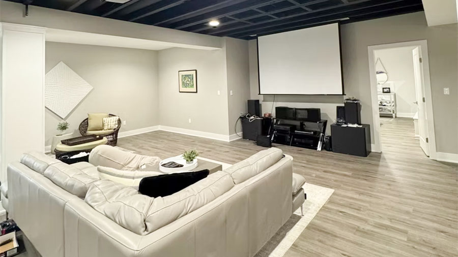 A finished basement with a leather couch and a projector screen.